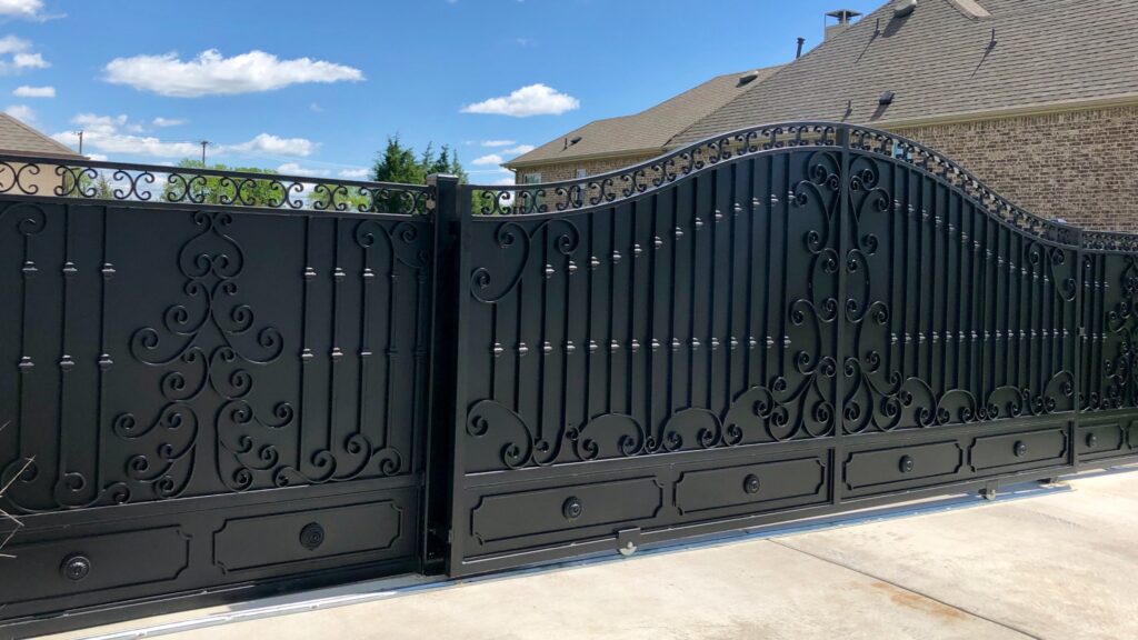 Elegant black wrought-iron gate with ornate designs, showcasing secure entrance to a residential property under a bright blue sky.