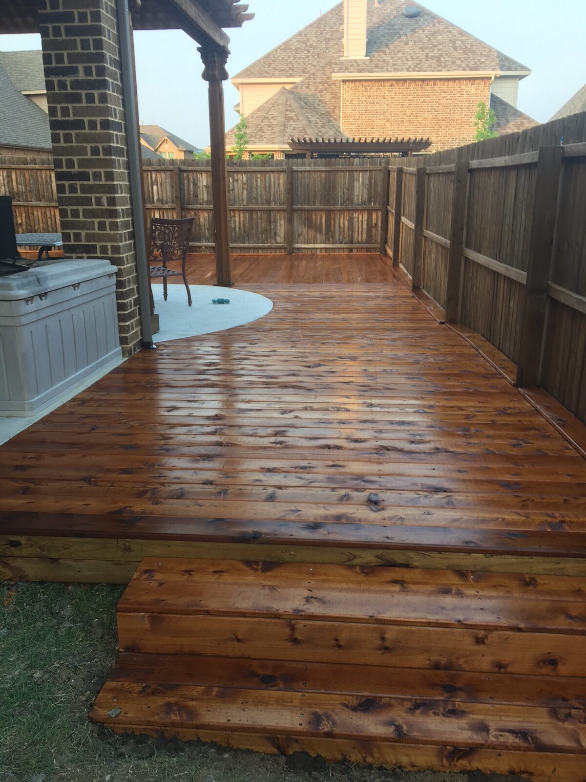 Shiny, newly finished wooden deck with steps leading down, surrounded by a fenced backyard and houses in the background. Perfect for outdoor relaxation.