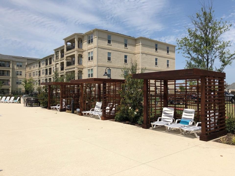 Modern poolside area featuring spacious cabanas with lounge chairs, adjacent to a multi-story residential building under a clear blue sky.